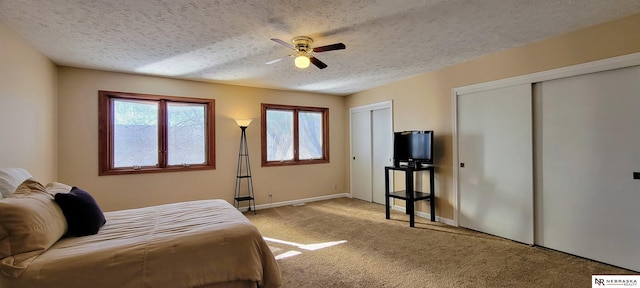 bedroom featuring two closets, light carpet, ceiling fan, a textured ceiling, and baseboards