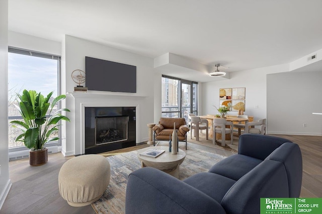 living area featuring a fireplace with flush hearth, visible vents, baseboards, and wood finished floors