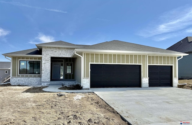 prairie-style home with a garage, a shingled roof, driveway, stone siding, and board and batten siding