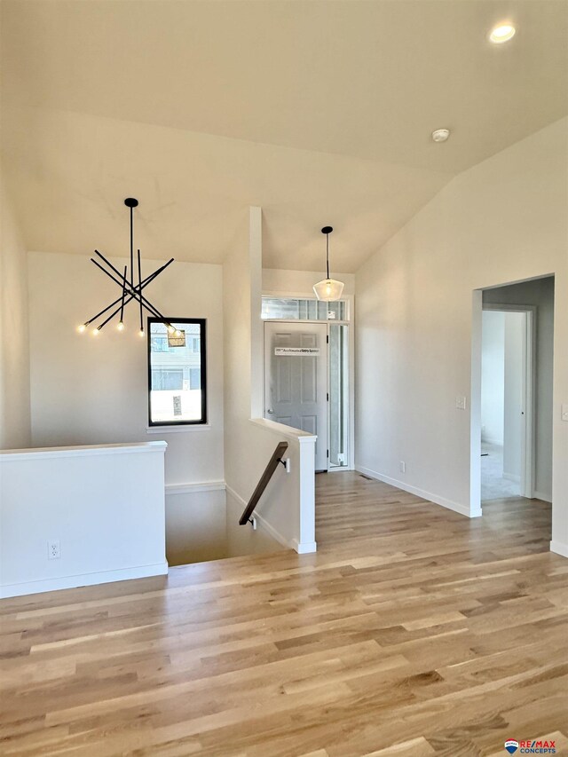 unfurnished room with light wood-style floors, lofted ceiling, a chandelier, and baseboards