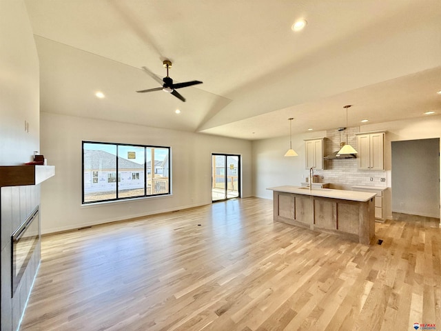 living area featuring light wood finished floors, a ceiling fan, a glass covered fireplace, vaulted ceiling, and recessed lighting