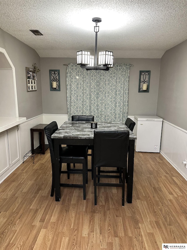 dining room featuring a notable chandelier, light wood-style flooring, a textured ceiling, and wainscoting