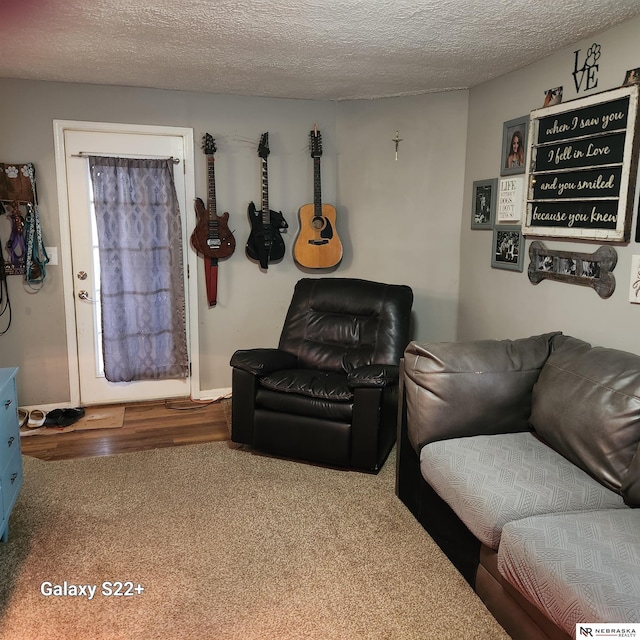 carpeted living area with a textured ceiling, baseboards, and wood finished floors