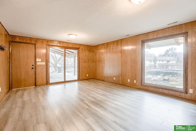 interior space with light wood-type flooring, wooden walls, visible vents, and a textured ceiling