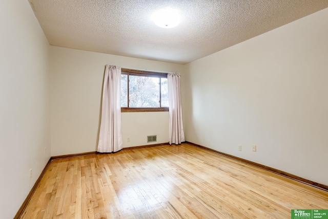 empty room with light wood-style floors, visible vents, baseboards, and a textured ceiling