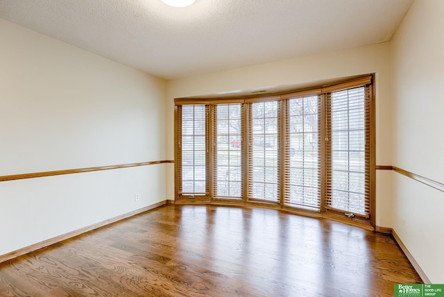 empty room featuring a textured ceiling, baseboards, and wood finished floors