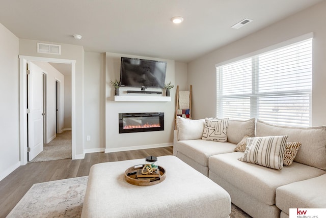 living area featuring a glass covered fireplace, wood finished floors, visible vents, and baseboards