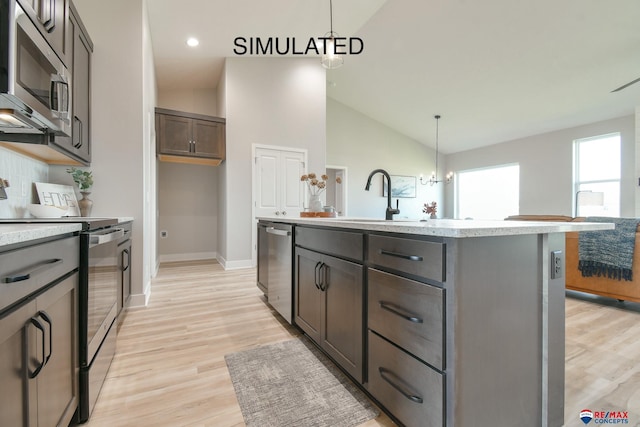 kitchen featuring a center island with sink, baseboards, appliances with stainless steel finishes, decorative light fixtures, and light wood-style floors