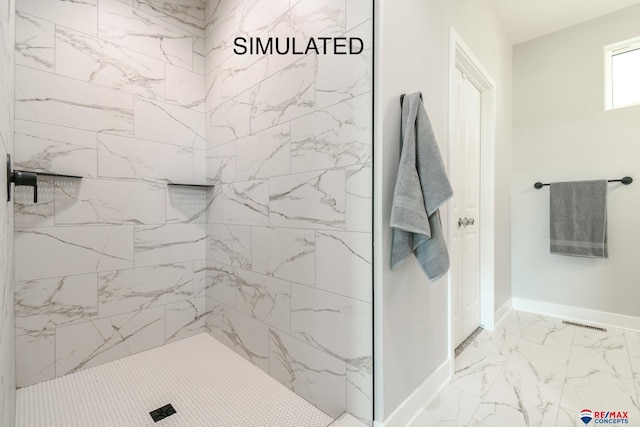 bathroom featuring marble finish floor, a tile shower, and baseboards