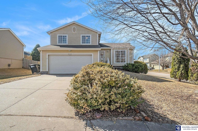 tri-level home featuring concrete driveway, an attached garage, and fence