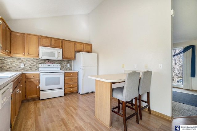 kitchen with tasteful backsplash, light countertops, a peninsula, light wood-style floors, and white appliances