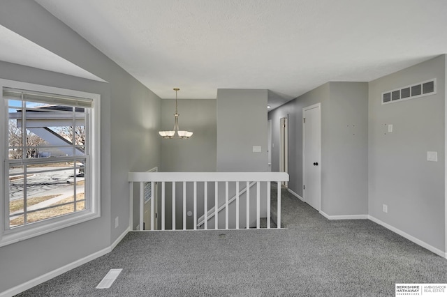 carpeted spare room with a notable chandelier, visible vents, a textured ceiling, and baseboards