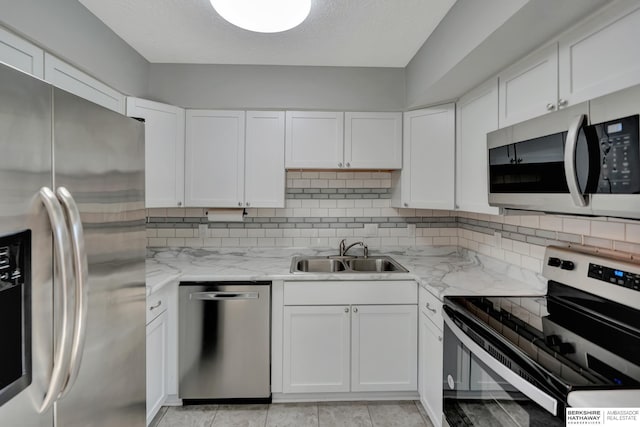 kitchen with backsplash, light stone counters, appliances with stainless steel finishes, white cabinetry, and a sink