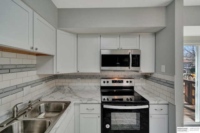 kitchen featuring electric range, a sink, stainless steel microwave, white cabinetry, and decorative backsplash