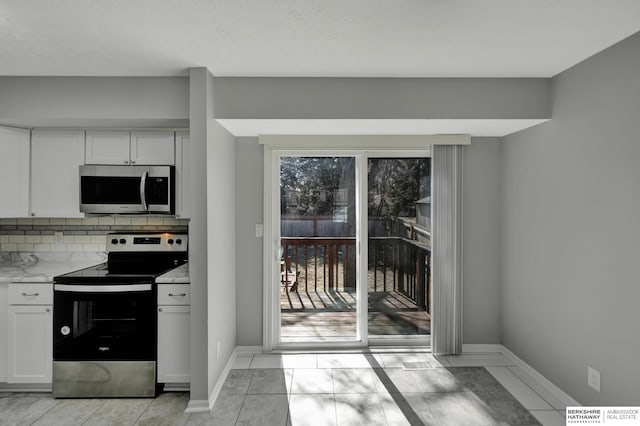 kitchen with a wealth of natural light, decorative backsplash, appliances with stainless steel finishes, and white cabinets