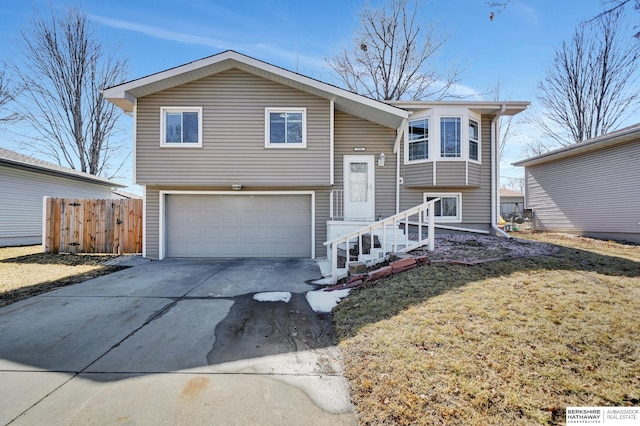 bi-level home featuring a garage, concrete driveway, a front lawn, and fence