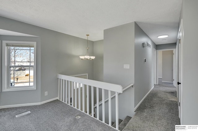 hallway with visible vents, a textured ceiling, baseboards, and carpet floors