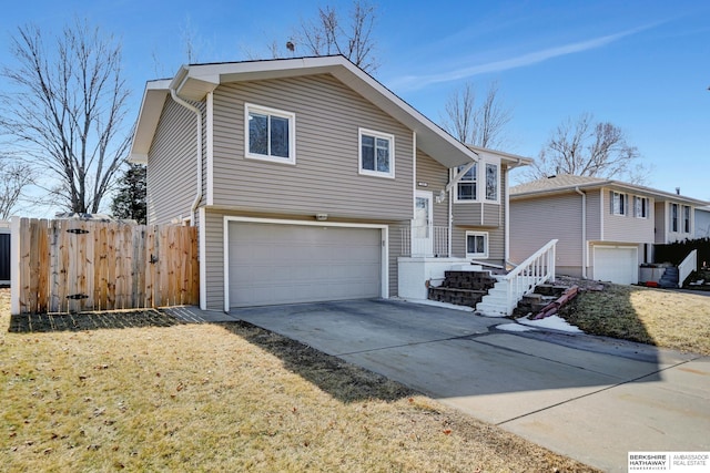 bi-level home featuring an attached garage, concrete driveway, and fence