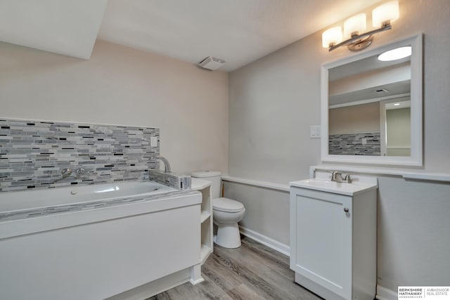 bathroom with vanity, wood finished floors, decorative backsplash, a garden tub, and toilet