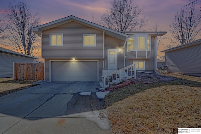 bi-level home featuring a garage, concrete driveway, and fence