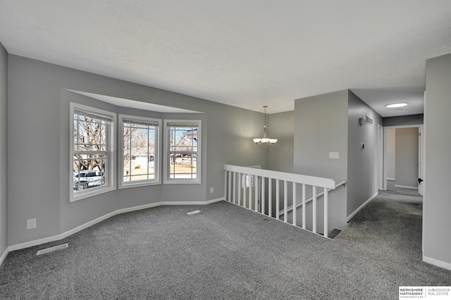 carpeted spare room featuring a chandelier, visible vents, and baseboards