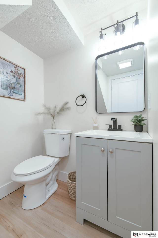 half bath with toilet, wood finished floors, vanity, and a textured ceiling