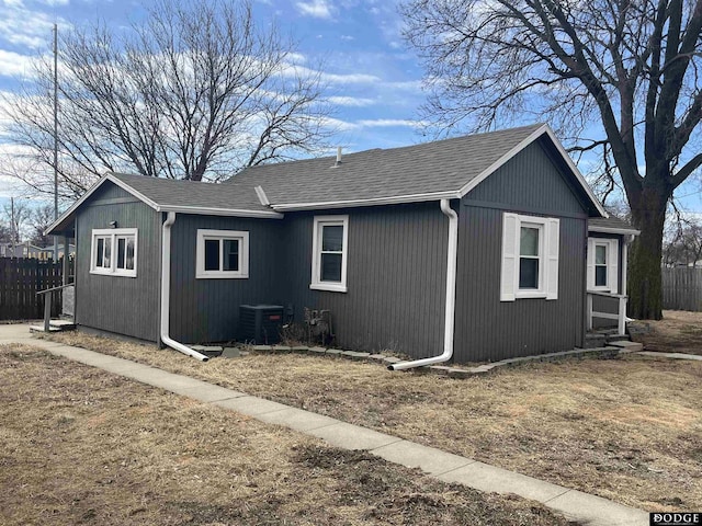 view of side of property featuring roof with shingles, fence, and central AC unit