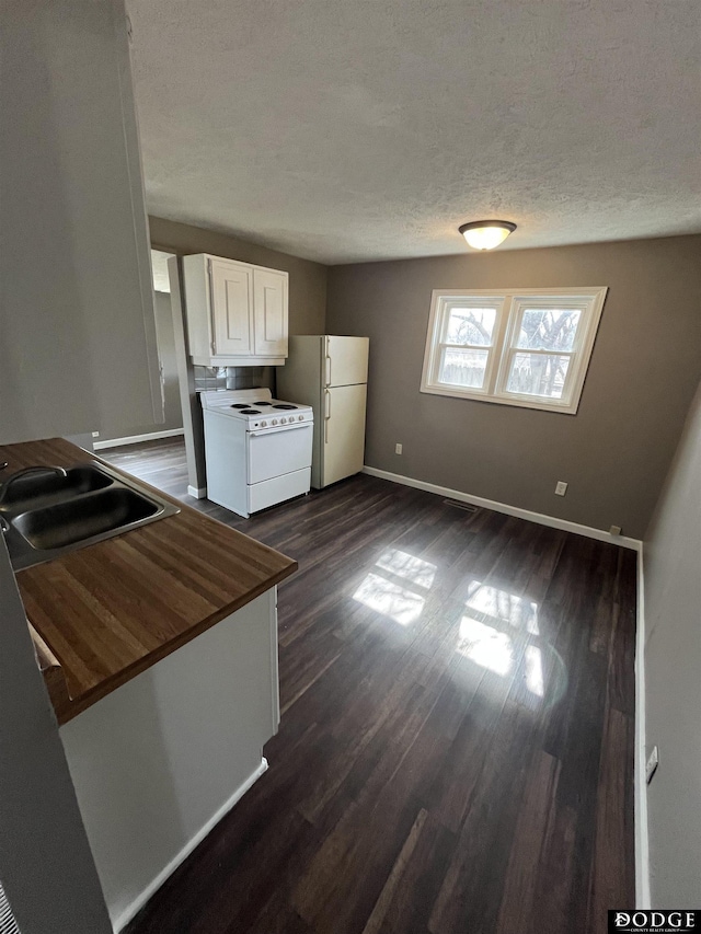 kitchen with dark wood-style flooring, a sink, a textured ceiling, white appliances, and baseboards