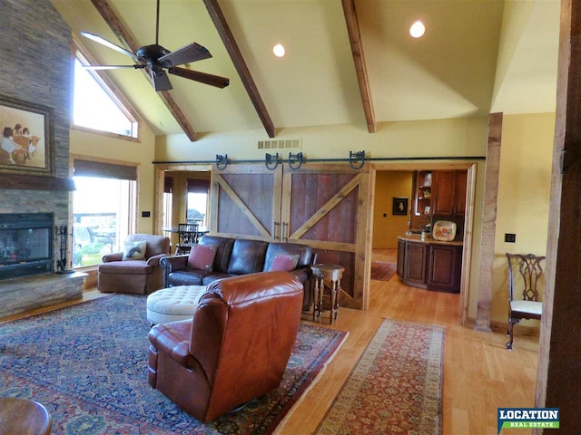 living room with beam ceiling, visible vents, light wood-style flooring, a barn door, and high vaulted ceiling