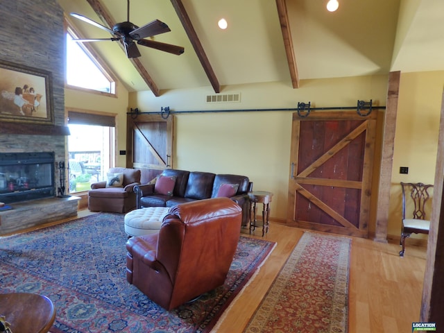 living area featuring a barn door, visible vents, a ceiling fan, wood finished floors, and beam ceiling