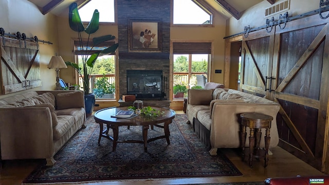 living room with a large fireplace, a barn door, a wealth of natural light, and wood finished floors