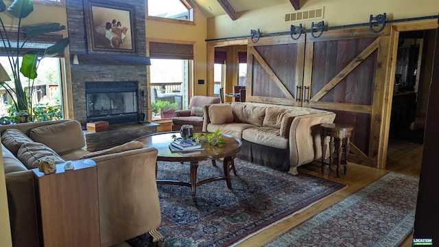 living area featuring a barn door, visible vents, wood finished floors, vaulted ceiling with beams, and a fireplace