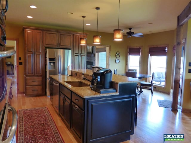 kitchen with light stone counters, pendant lighting, a center island with sink, light wood finished floors, and a sink