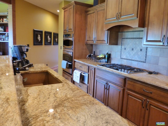 kitchen featuring appliances with stainless steel finishes, brown cabinets, light stone counters, backsplash, and a warming drawer