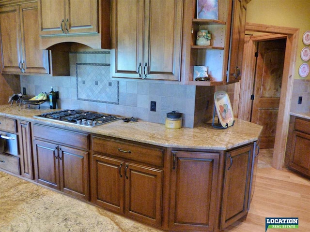 kitchen featuring stainless steel gas stovetop, backsplash, and light wood finished floors