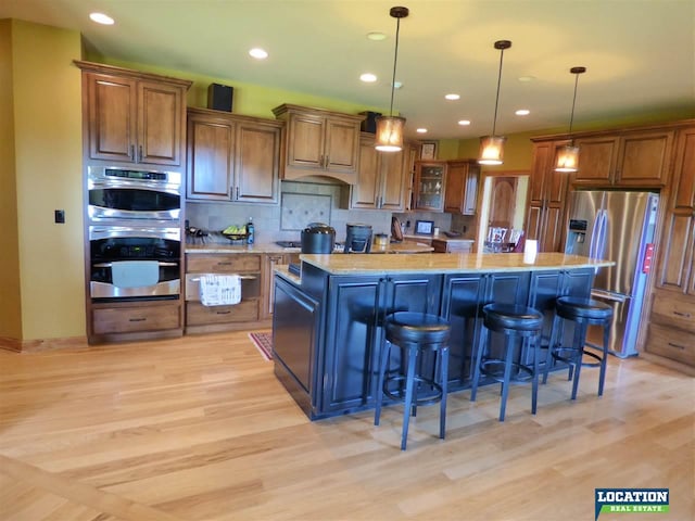 kitchen featuring stainless steel appliances, a kitchen island, light wood-type flooring, brown cabinets, and decorative backsplash