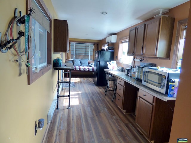 kitchen with dark wood-style flooring, a wall unit AC, light countertops, stainless steel microwave, and freestanding refrigerator