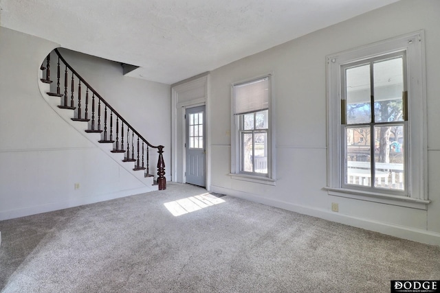 carpeted foyer entrance featuring a textured ceiling, baseboards, and stairs