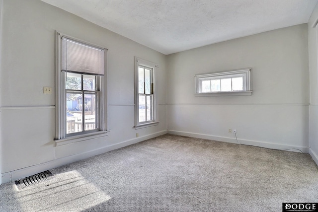 carpeted spare room with a textured ceiling, visible vents, and baseboards