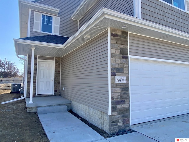 view of exterior entry with cooling unit, stone siding, and an attached garage