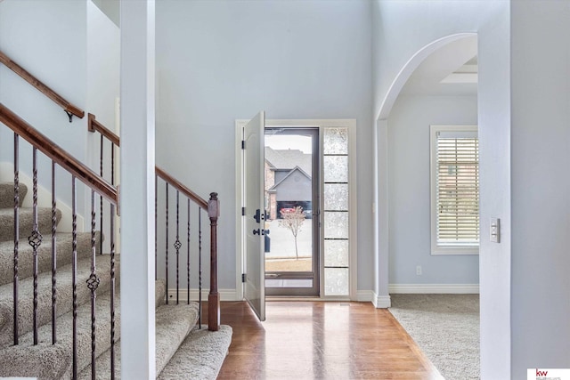 entrance foyer featuring stairs, baseboards, arched walkways, and wood finished floors