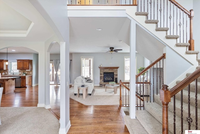 entryway with a stone fireplace, stairway, light wood-style flooring, and a ceiling fan