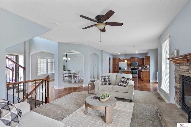 living room with stairway, arched walkways, a stone fireplace, and wood finished floors