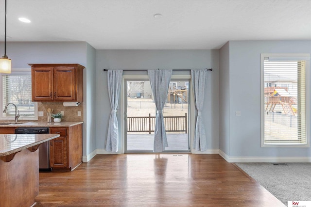 kitchen with brown cabinets, tasteful backsplash, a sink, wood finished floors, and dishwasher