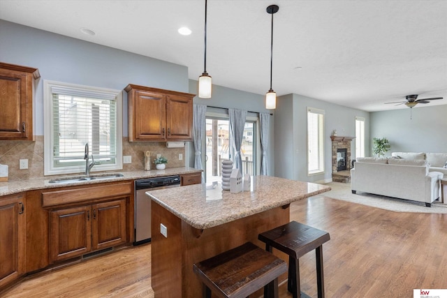 kitchen featuring open floor plan, stainless steel dishwasher, brown cabinetry, and a sink