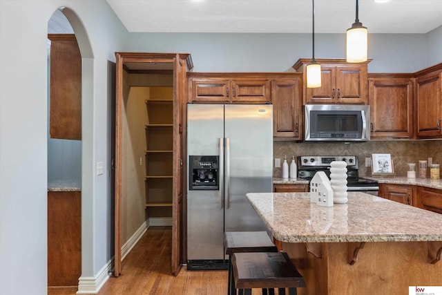 kitchen with a breakfast bar, brown cabinetry, stainless steel appliances, and backsplash