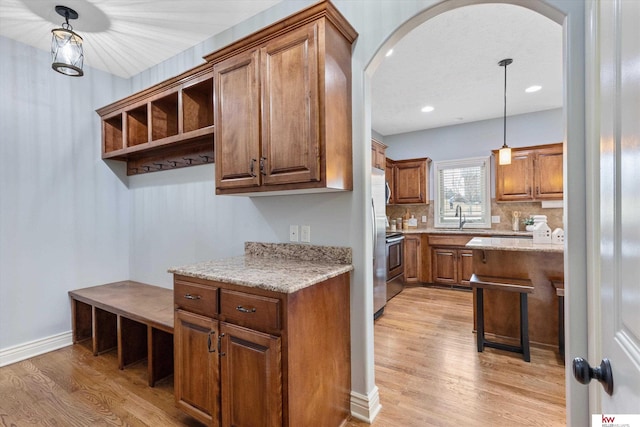 kitchen featuring arched walkways, brown cabinets, open shelves, a sink, and light wood-type flooring