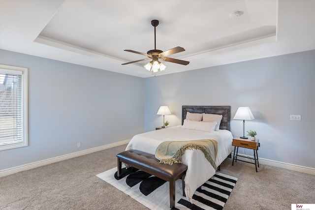 carpeted bedroom with baseboards, a tray ceiling, and a ceiling fan