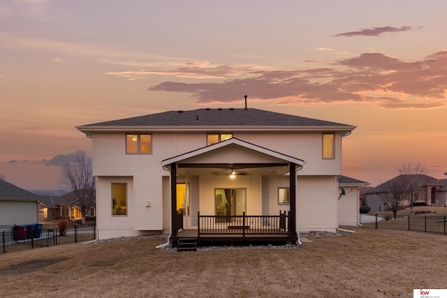 back of house at dusk with a fenced backyard, a lawn, a ceiling fan, and a wooden deck