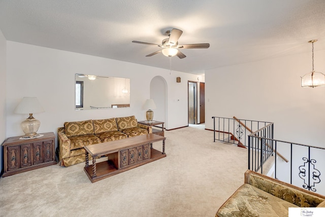 living area featuring light carpet, a textured ceiling, arched walkways, and a ceiling fan